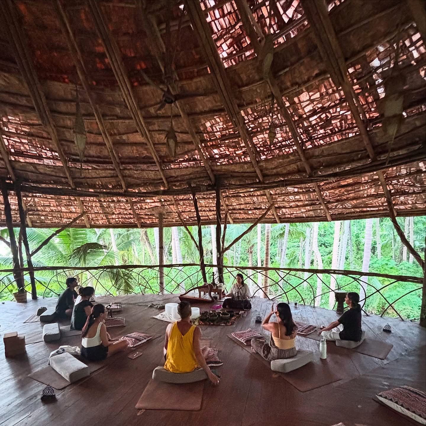 Guided circle session in an open-air bamboo pavilion surrounded by palm trees